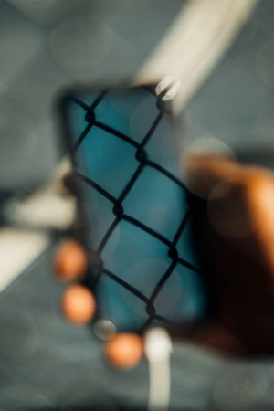 Close-up shot of a person holding a blurred smartphone with chain-link reflection, creating an abstract and textured visual effect.