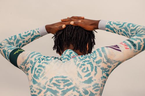Back view of an adult male with dreadlocks wearing a patterned cycling jersey and holding his hands behind his head.