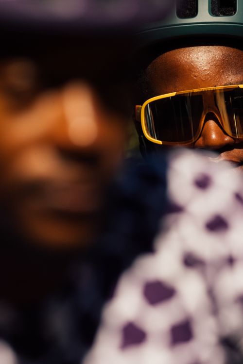 Close-up of a cyclist wearing a helmet and yellow sunglasses with another person in the blurred background.