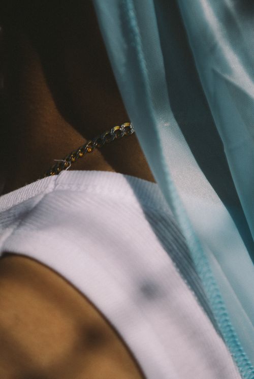 Close up of a person's neck, wearing a white shirt and necklace, draped with a sheer blue fabric, creates a soft and intimate mood.