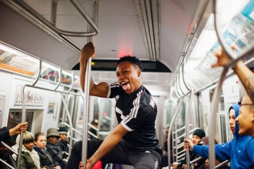 Enthusiastic man performs on a subway pole surrounded by other passengers in an indoor train car with silver and white interior.