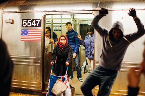 People boarding a subway train with an American flag visible on the train exterior, creating a candid urban scene.