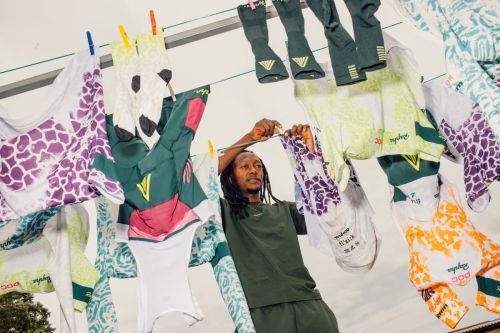 Man hanging colorful athletic apparel, including cycling jerseys and socks, on a clothesline against a neutral backdrop.