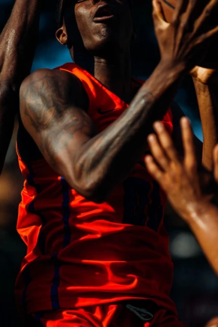 Action shot of an African American adult male basketball player reaching for a ball while wearing an orange uniform on the court.