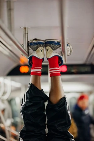 A person's legs and feet, wearing sneakers and red striped socks, are elevated towards the ceiling of a public train car.