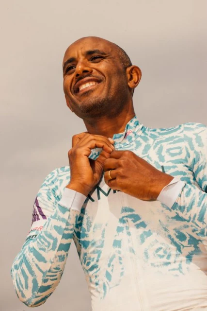 Cyclist adjusts jersey with abstract design in outdoor setting; man smiles, showcasing athletic apparel for sport and active lifestyle content.