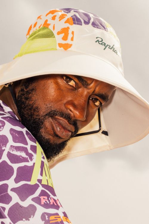 Black man wearing a patterned bucket hat and colorful athletic jersey, photographed in New York.