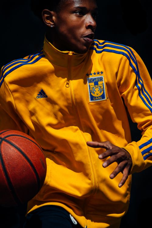 Young adult male in yellow jacket holds basketball. Dark studio background. Focused on person, sports attire, and athletic equipment.