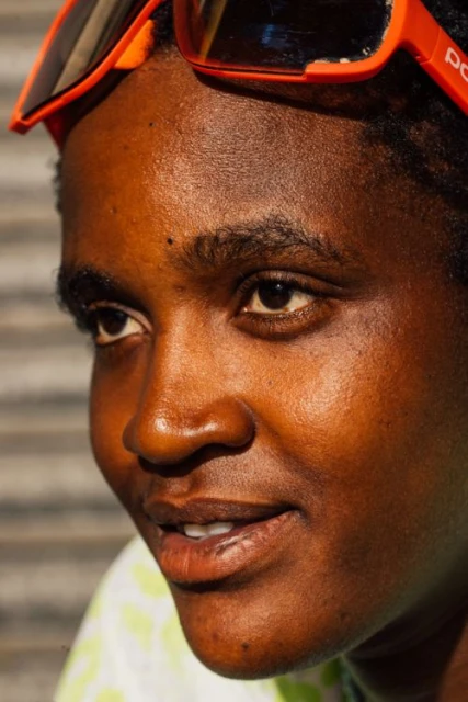 Close-up portrait of a dark-skinned adult woman with sunglasses on her head, looking off-camera with natural light and shallow depth of field.