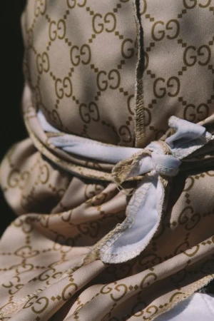 Close-up of a person wearing a beige monogram-patterned durag tied with a white headband, photographed by Alessandro Simonetti.