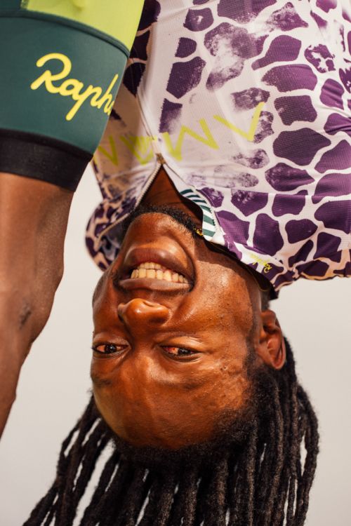 Upside-down view of smiling African American man wearing a patterned cycling jersey and dark green cycling shorts with logo.
