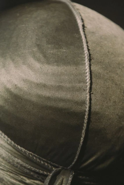 Close-up of a textured olive green du-rag with a vertical seam and subtle tie-dye effect, set against a dark, gradient background.