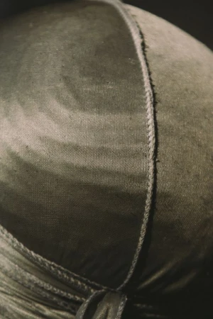 Close-up of a textured olive green du-rag with a vertical seam and subtle tie-dye effect, set against a dark, gradient background.