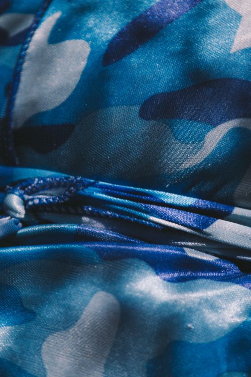 Close-up of fabric with a blue and white camouflage pattern, showing folds and a knotted drawstring detail.