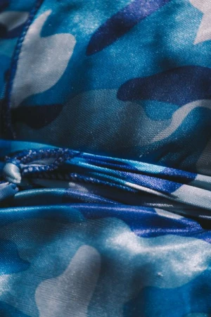 Close-up of fabric with a blue and white camouflage pattern, showing folds and a knotted drawstring detail.