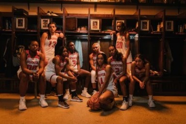 Group of nine female basketball players in white uniforms inside a wooden locker room by Alessandro Simonetti