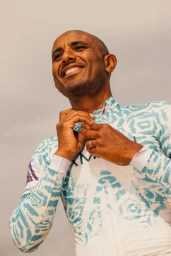 Bald man wearing a white and blue patterned athletic jersey zipping it up outdoors