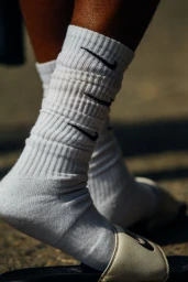 Close-up of legs wearing ribbed white athletic socks with black logos and slip-on sandals outdoors