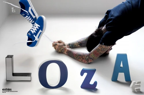 Skateboarder in a downward dog yoga pose with tattooed arms between blue Etnies shoes and block letters spelling out 'LOZA' in a white room.