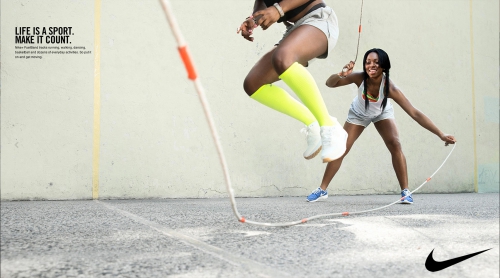 Two Black women jumping rope outdoors on pavement wearing athletic clothing and smiling, promoting sport and fitness.