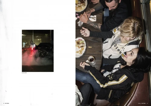 Overhead shot of three adults at a table with food and drinks, illuminated by bright lighting, alongside a nighttime street scene with a motorcycle.