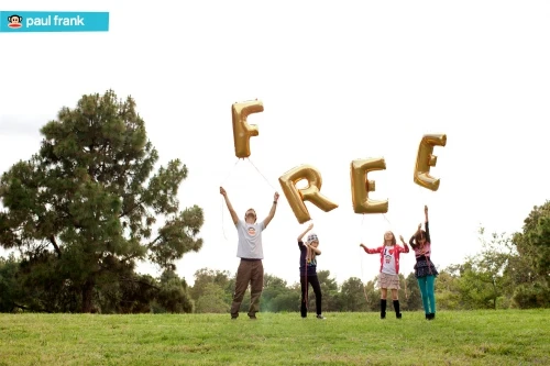 Four children and one adult on grassy field holding gold letter balloons that spell 'FREE' in outdoor daytime setting.