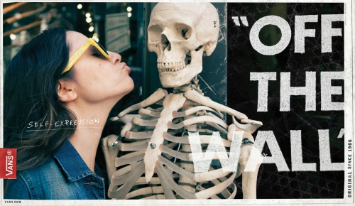 A woman with yellow sunglasses puckers her lips toward a skeleton with an Off the Wall Vans sign in the background, promoting self-expression.