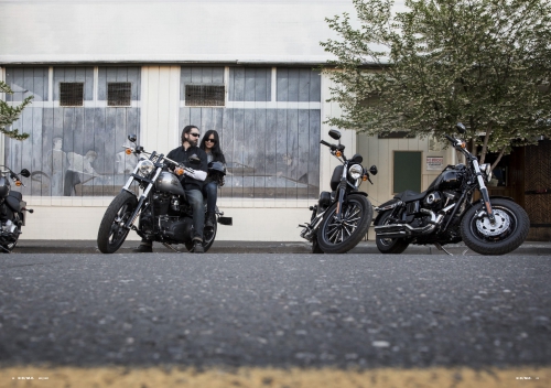 Low-angle shot of two people on a motorcycle parked on a street next to two other motorcycles in front of a building.