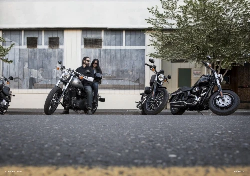 Low-angle shot of two people on a motorcycle parked on a street next to two other motorcycles in front of a building.