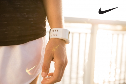 Close-up of a person wearing a fitness tracker and white athletic shorts with the Nike logo, set against a bright background.