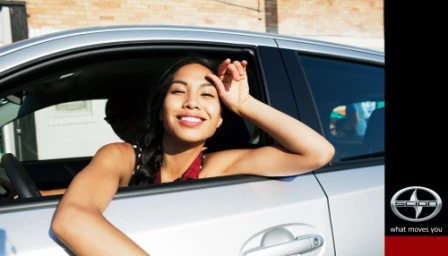 Smiling young woman leaning out of a silver car window in Los Angeles by photographer Rennie Solis.