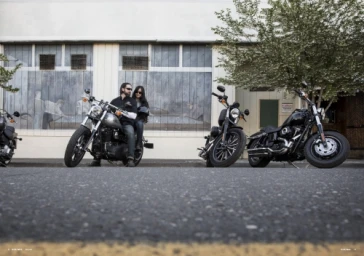 Low-angle shot of two people on a motorcycle parked on a street next to two other motorcycles in front of a building.