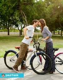 A young couple standing outdoors near bicycles, smiling at each other in a park setting.