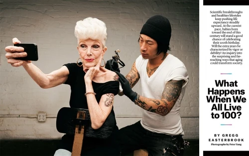 Elderly woman takes a selfie as a tattoo artist works on her shoulder tattoo in a bright indoor studio. Beauty and lifestyle concept.