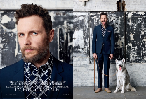 Portrait of adult male in blue suit next to a husky dog in front of an industrial background with dark and light colors.