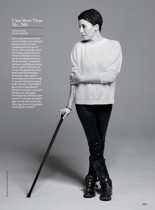 Black and white portrait of Sarah Eyre, an adult woman with short dark hair, wearing a white sweater, black leggings, and boots, using a cane.