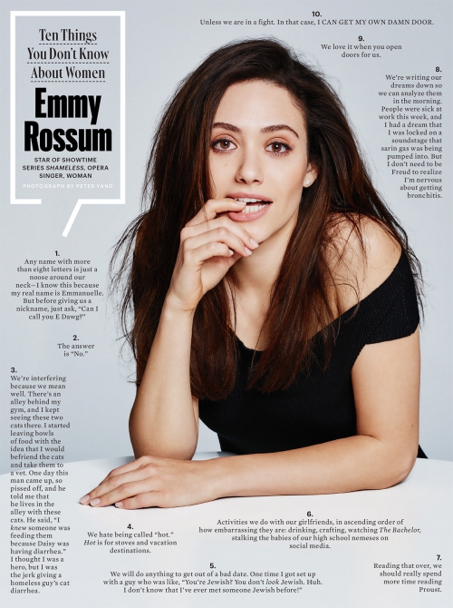 Portrait of Emmy Rossum, star of Shameless, posing in a black top with her fingers near her lips, in a studio illuminated by bright lighting.