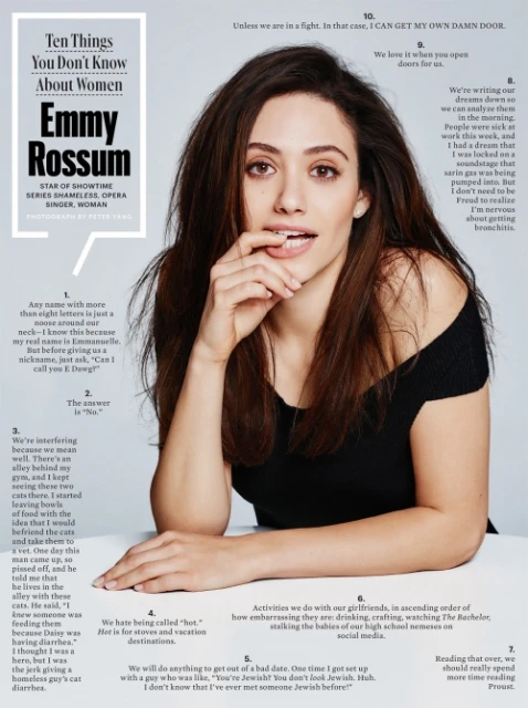 Portrait of Emmy Rossum, star of Shameless, posing in a black top with her fingers near her lips, in a studio illuminated by bright lighting.