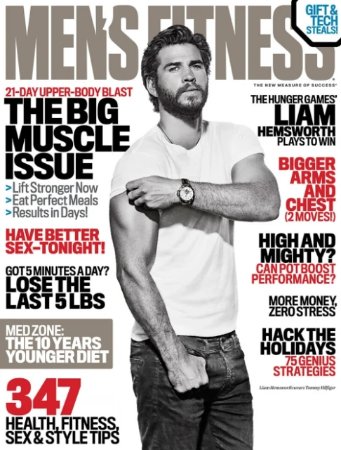 Liam Hemsworth on Men's Fitness magazine cover. Close-up of an adult man with a beard and short hair wearing a white t-shirt and jeans.
