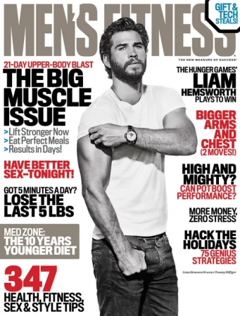 Liam Hemsworth on Men's Fitness magazine cover. Close-up of an adult man with a beard and short hair wearing a white t-shirt and jeans.
