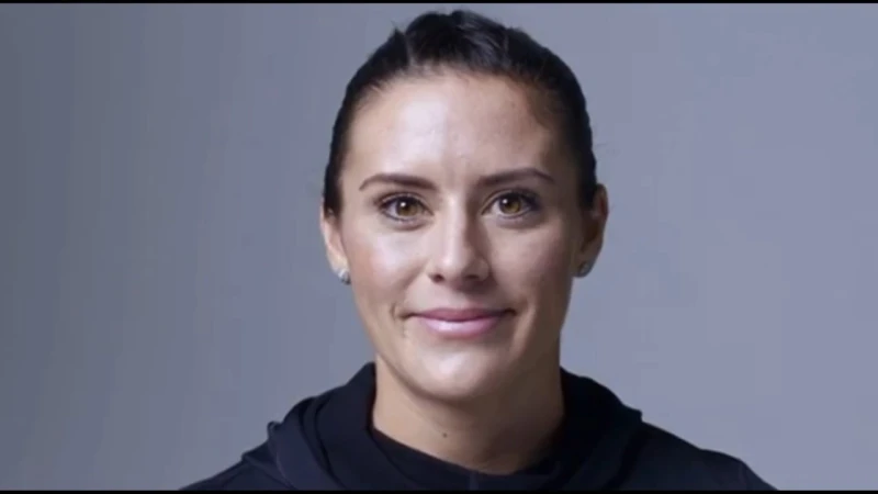 Portrait of a woman with dark hair tied back wearing a black top against a plain grey background