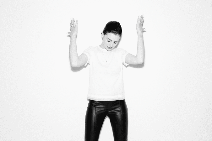 Anne Hathaway in a white t-shirt and black pants posing with hands raised against a white background by Peter Yang