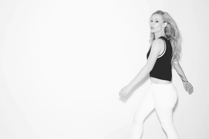 Iggy Azalea wearing a black sleeveless top and white jeans posing against a plain white background in a portrait by Peter Yang.