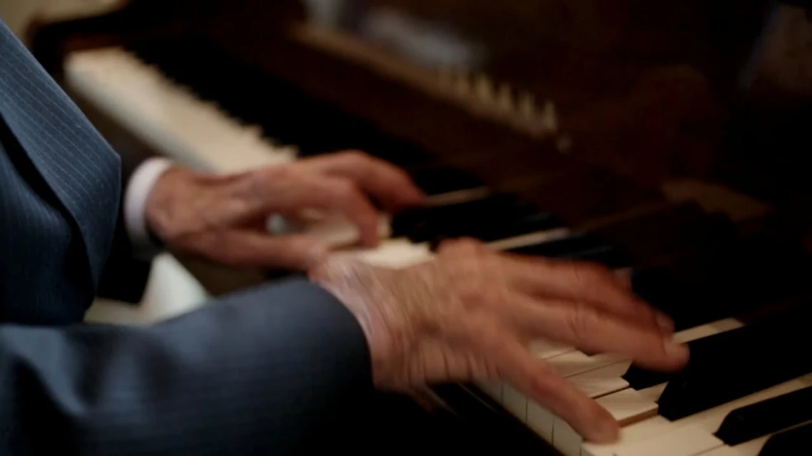 Close-up of an elderly person's hands playing a piano, with a focus on the musical instrument and the musician's fingers in motion.