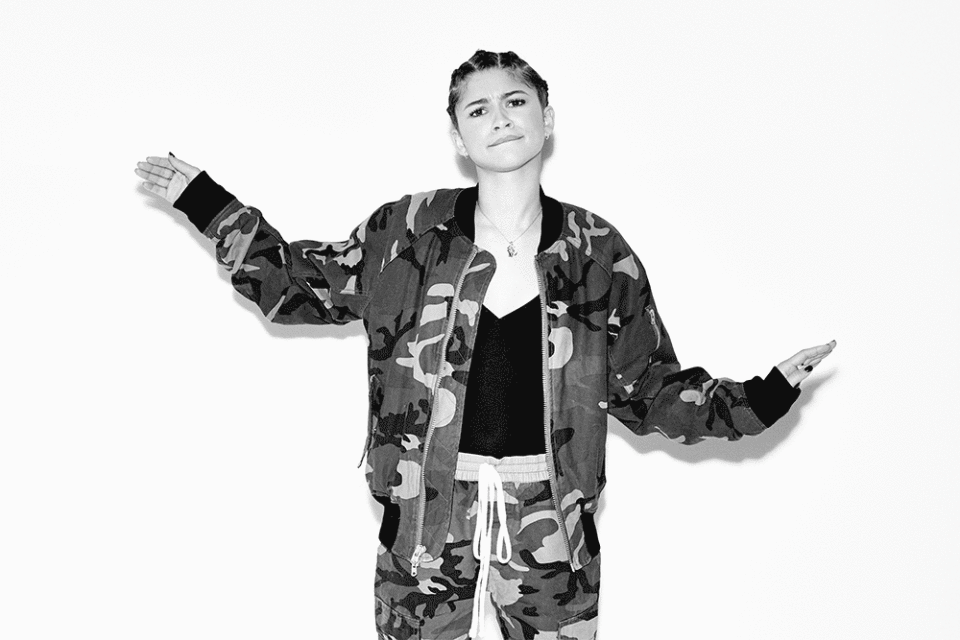 Black-and-white portrait of a female adult wearing a camouflage jacket and pants, with her arms extended to both sides against a white background.