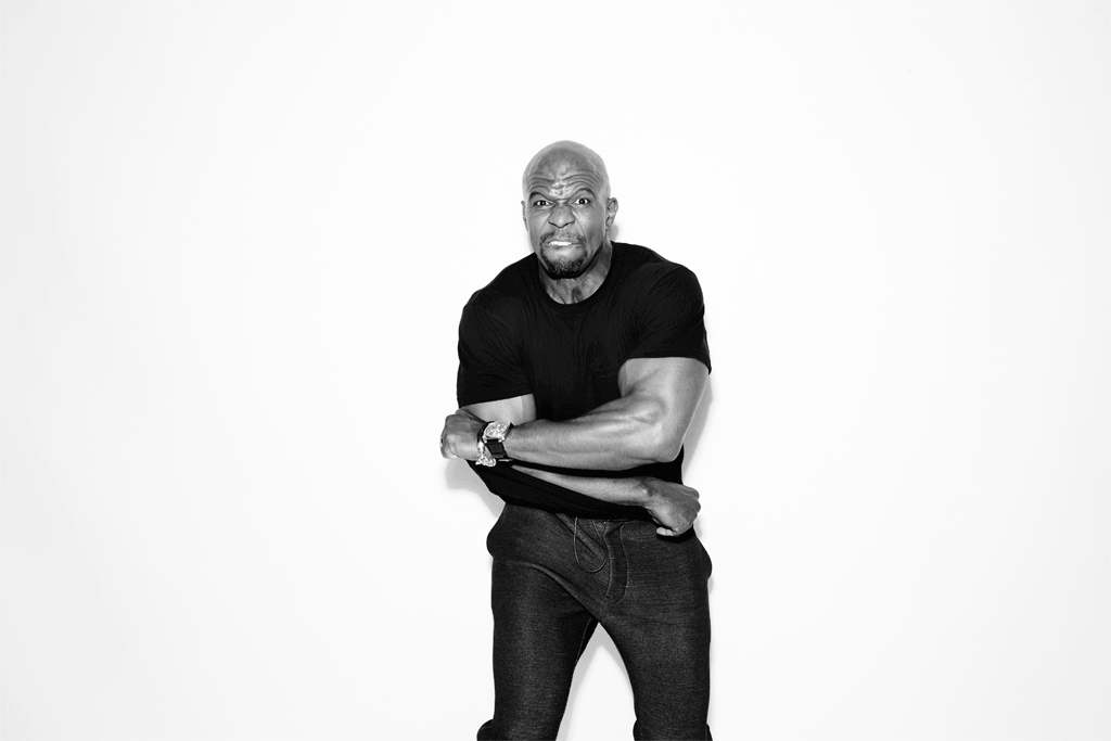 Black and white portrait of an adult male with muscular build and an intense facial expression, wearing a dark t-shirt and jeans indoors.