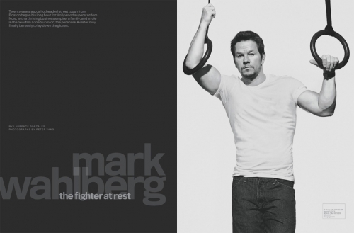 Black and white portrait of Mark Wahlberg, wearing a white t-shirt and blue jeans, suspended from gymnastic rings against a plain white background.