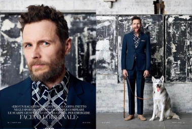 Editorial portrait of a bearded man in a blue suit and patterned shirt standing next to a husky dog