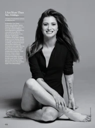 Portrait of a smiling woman seated against a seamless grey studio backdrop wearing a dark buttoned shirt