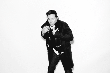 Portrait of Jimmy Fallon wearing a black duffel coat against a plain white background, photographed by Peter Yang.
